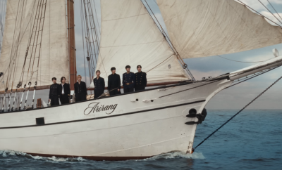All seven members of BTS standing in a row at the prow of a sailing ship